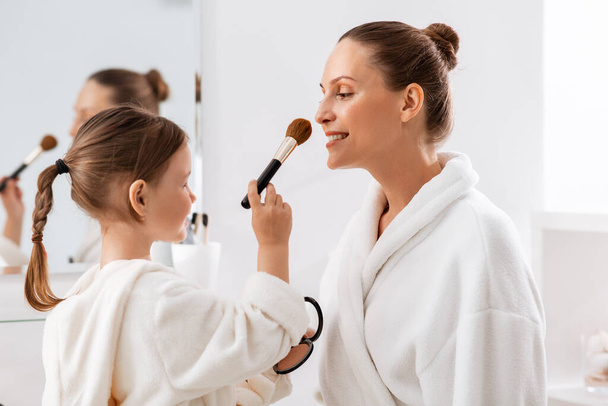 beauty, family and people concept - happy smiling mother and little daughter with brush and powder applying make up in bathroom - Фото, зображення