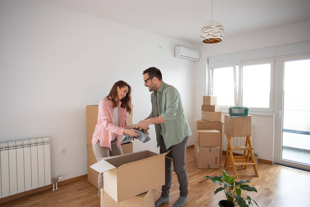 Joven pareja feliz desempacando sus pertenencias de una caja de cartón en su nuevo apartamento. - Foto, Imagen