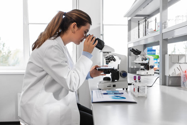 science research, work and people concept - female scientist with microscope working in laboratory - Fotoğraf, Görsel