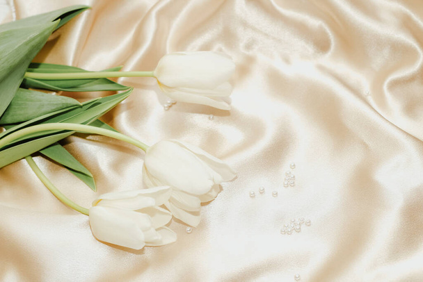 Bouquet of white tulips with pearl beads on silk golden nude satin background. - Foto, imagen