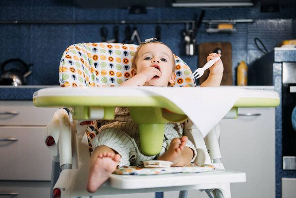 Babys first solid food. Solid food for little child 6 months old. Cute smiling baby girl in high chair eats and tastes with fingers various solid food. Healthy child nutrition - Foto, Imagen