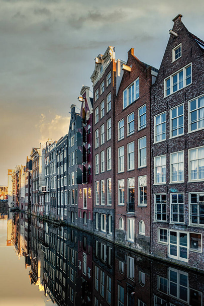 Amsterdam City Scene,  typical dutch houses and their reflection in the canal. Old 17th and 18th century brick houses along a canal in centre of Amsterdam, Netherlands. - Photo, Image