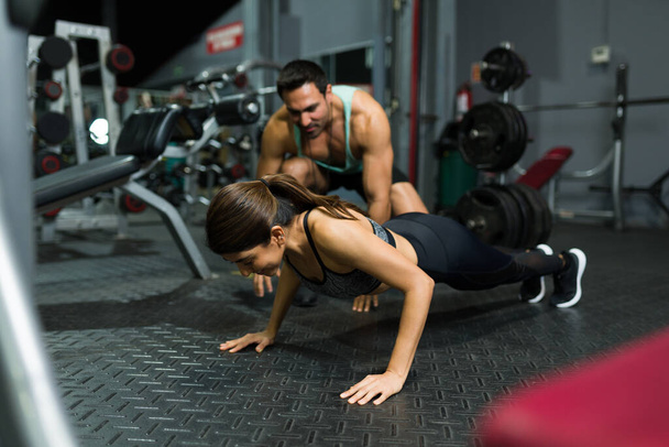 Sporty young woman doing push ups with the assistance of her workout trainer at the gym - Photo, Image