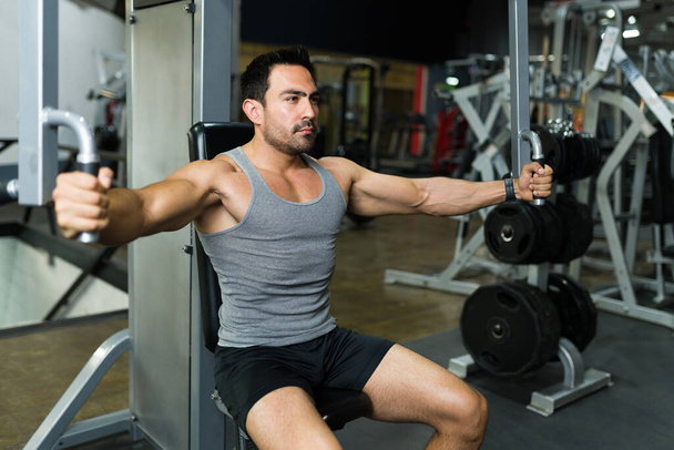 Starker lateinischer Mann trainiert ihre Rückenmuskulatur mit einem Fitnessgerät  - Foto, Bild