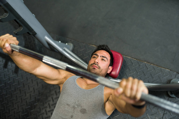 Skupiony atrakcyjny mężczyzna poci się podczas podnoszenia ciężarów na siłowni. Trening i ćwiczenie trenera fitness - Zdjęcie, obraz
