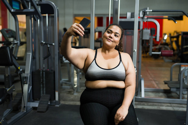 Gyönyörű elhízott nő mosolyog és csinál egy szelfit egy okostelefonnal, hogy posztoljon egy képet a közösségi média edzés után - Fotó, kép