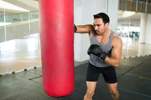 Un joven fuerte entrenando para un concurso de boxeo. Atlético hombre guapo golpeando una bolsa de boxeo - Foto, Imagen