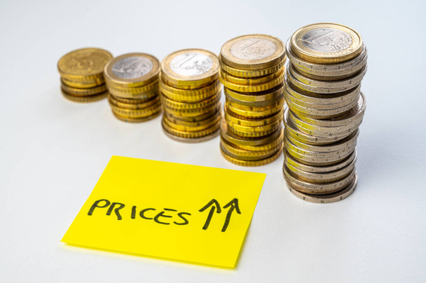 Pilhas de moedas de altura crescente, ao lado de um bilhete amarelo e a palavra "preços". Aumento de preços. - Foto, Imagem