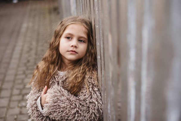 Портрет ребенка на городской улице. Маленькая девочка в городской обстановке с грустными глазами смотрит в камеру - Фото, изображение