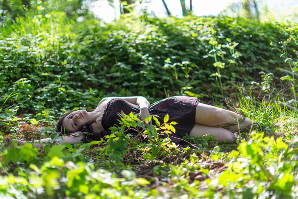 ブルネットの女の子は茶色のドレスのない体でツタの牧草地に横たわっています。高品質の写真 - 写真・画像