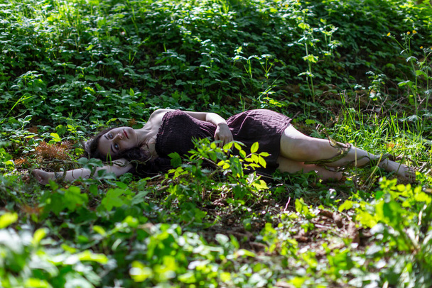 brunette girl lying in ivy meadow with brown dress lifeless body. High quality photo - Zdjęcie, obraz