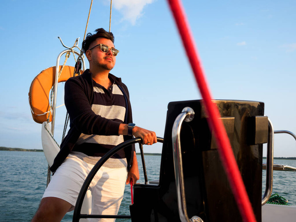 handsome black hair person steering wheel sailing yacht or sailboat on a vacations - Fotografie, Obrázek