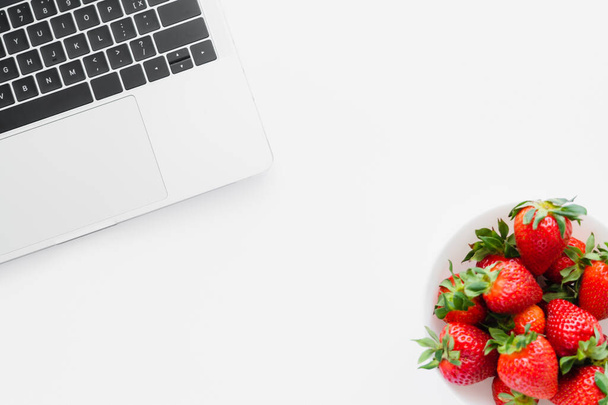 Draufsicht auf natürliche Erdbeeren in der Nähe von Laptop auf weißem Hintergrund - Foto, Bild