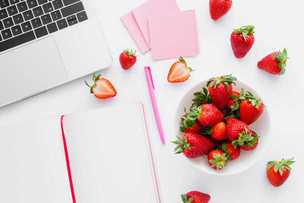 Top view of organic strawberries near laptop and notebook on white background - Foto, afbeelding