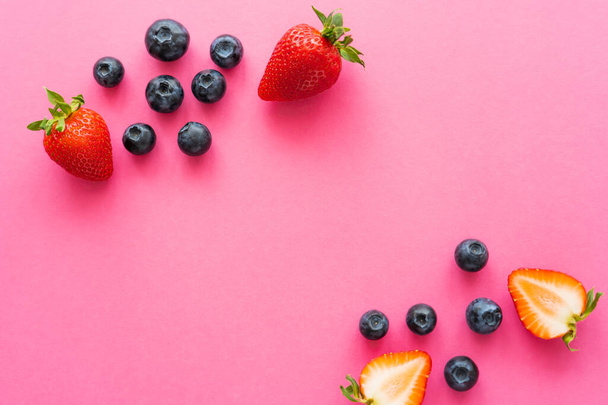 Top view of strawberries and whole blueberries on pink surface  - Foto, afbeelding