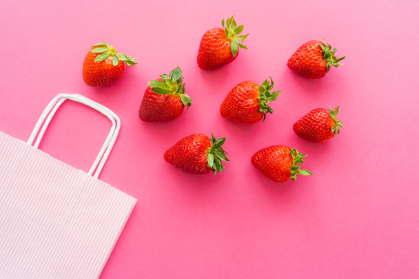 Vue de dessus des fraises fraîches avec des feuilles près du sac à provisions sur fond rose  - Photo, image