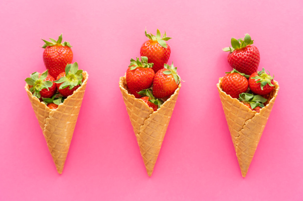 Poser à plat avec des fraises dans des cônes de gaufres sur fond rose  - Photo, image