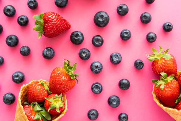 Flat lay with blueberries near strawberries in waffle cones on pink background  - Foto, immagini