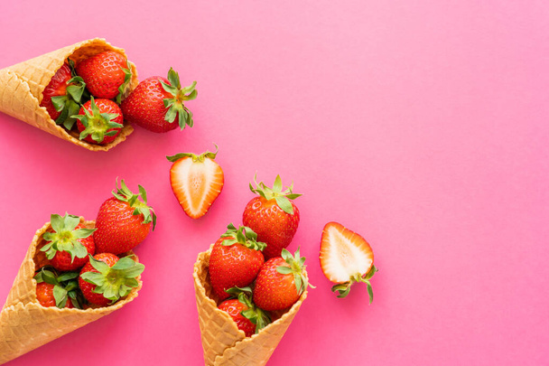 Top view of sweet strawberries with leaves in waffle cones on pink background  - Foto, imagen