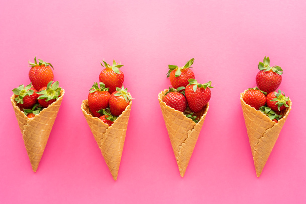 Flat lay with ripe berries with leaves in waffle cones on pink background  - Fotografie, Obrázek