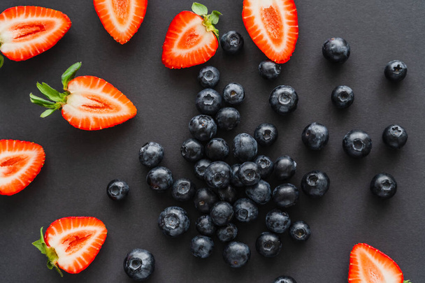 Vue de dessus des bleuets entiers et des fraises coupées sur fond noir  - Photo, image