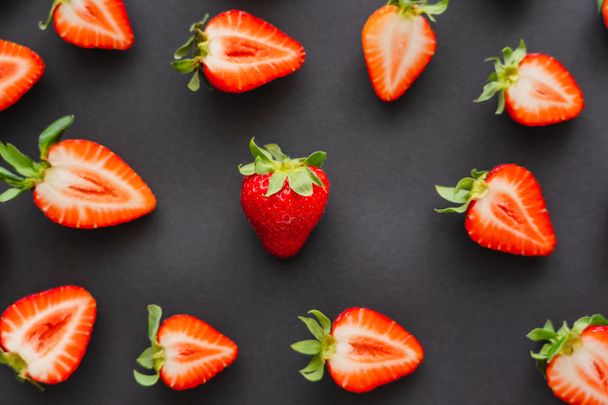 Flat lay with whole strawberry near cut berries on black background  - 写真・画像