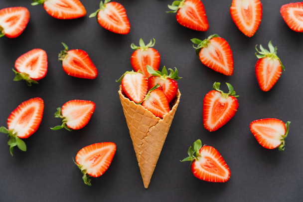 Flat lay with cut strawberries in waffle cone on black background  - Photo, Image