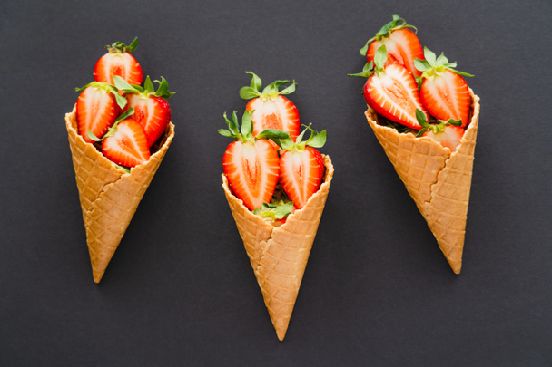 Top view of ripe cut strawberries in waffle cones on black background  - Photo, image