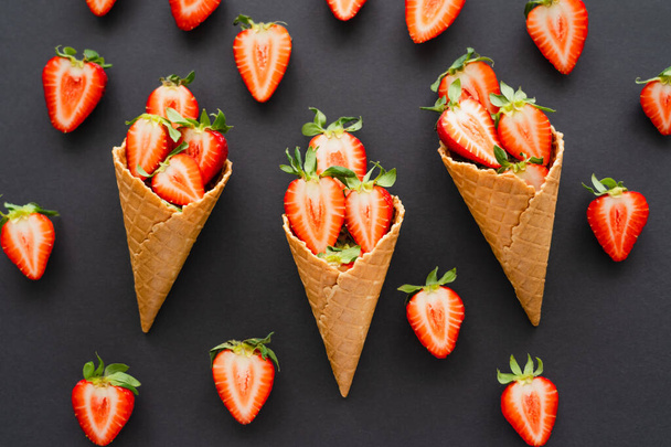 Flat lay of tasty strawberries and waffle cones on black background  - Fotó, kép