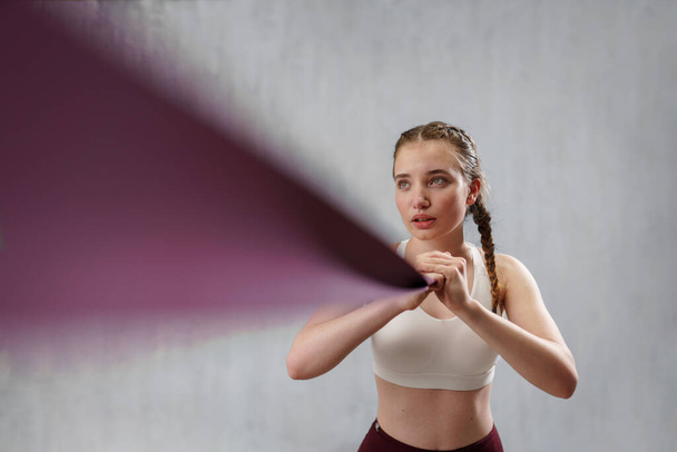 A sports woman in fashion sportswear exercising with elastic band stretch over greay background. - Foto, immagini