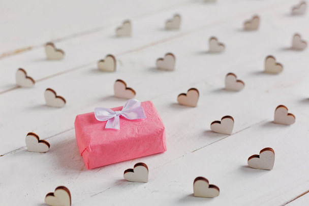 Pequeño regalo envuelto en papel rosa, corazones decorativos alrededor del regalo sobre fondo blanco. San Valentín, Día de la Mujer, Día de la Madre. - Foto, Imagen