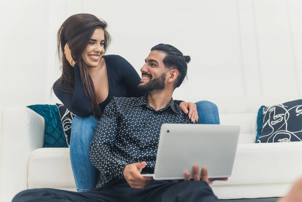 Yetişkin bir çift dizüstü bilgisayar kullanıyor ve evde otururken gülümsüyor, romantik bir ruh hali içinde. - Fotoğraf, Görsel