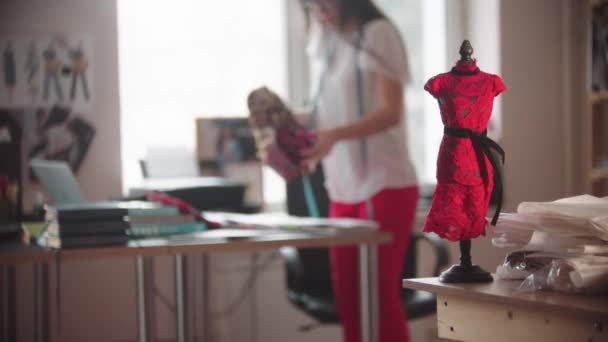 Eine kleine Auswahl eines Kleides auf einer kleinen Schaufensterpuppe und einer Frau, die in einem Designstudio arbeitet - Filmmaterial, Video