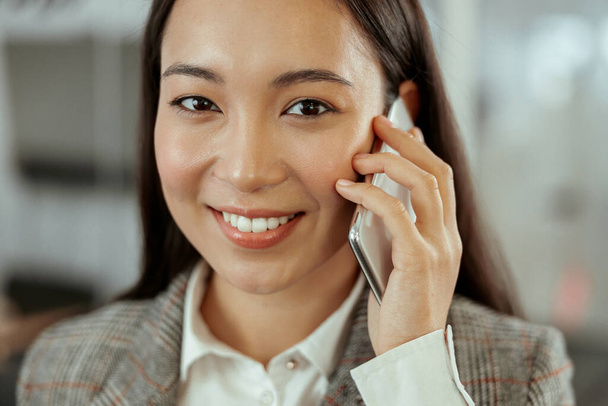 Közel egy mosolygó ázsiai üzletasszonyhoz, aki az irodában telefonál. Kiváló minőségű fénykép - Fotó, kép