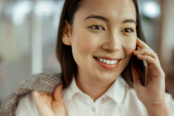 Close up of smiling asian business woman making phone call standing at office. High quality photo - Photo, Image