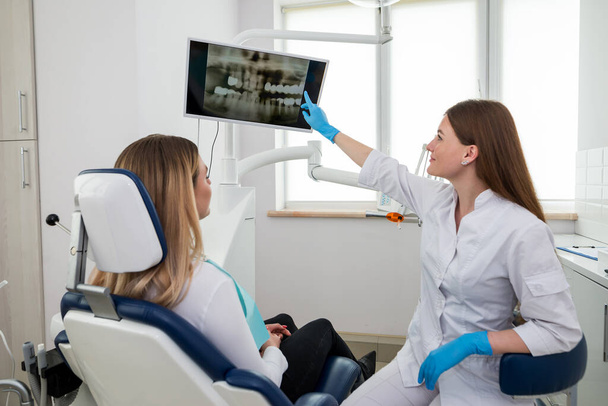 Dentista feminina mostrando raio-X dos dentes para paciente na clínica - Foto, Imagem