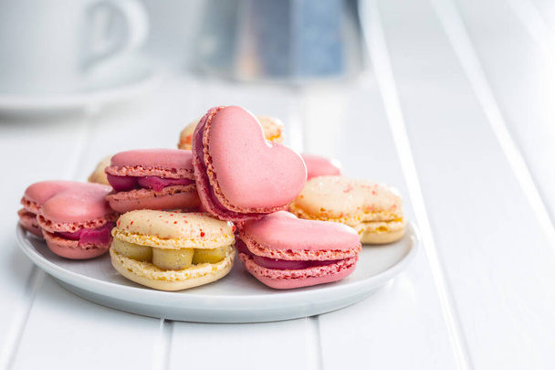 Heart shaped Sweet macarons on plate on a white table. - Фото, изображение