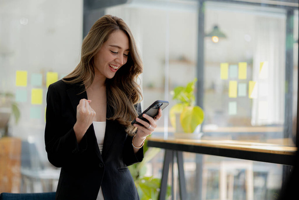 Woman gesturing and looking at the mobile phone, business woman checking company monthly sales and pretending to be happy as sales meet planned targets according to policy. Sales management concept. - Photo, image
