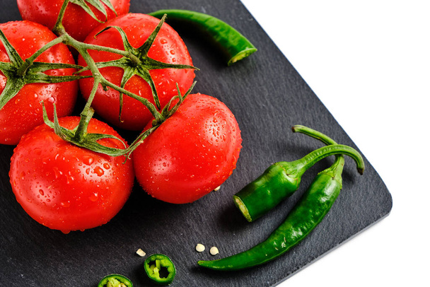 Tomatoes and pod of hot pepper on slate cutting board, isolated white background - Foto, immagini