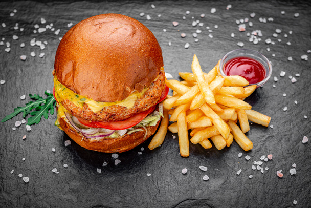 Frischer saftiger Burger mit Bratkartoffeln vor dunklem Hintergrund in einem Café. - Foto, Bild