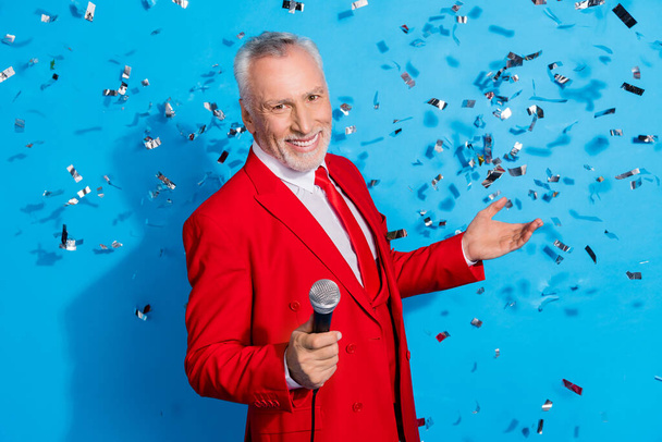 Photo of positive man hold mic confetti fall perform song wear red tuxedo isolated blue color background. - Foto, Imagem