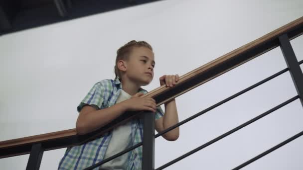Curious school child standing stairway alone at break. Preteen schoolboy leaning on railings examine hall. Serious interested boy look attentively inspecting school corridor. Modern childhood concept. - Footage, Video