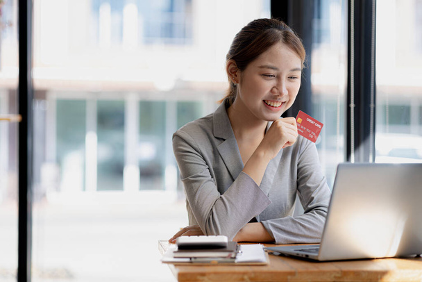 Beautiful woman holding a credit card, she uses a credit card to pay for goods and services online, the concept of using a credit card for online shopping, ordering goods and services on the website. - 写真・画像