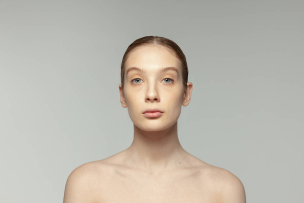 One young girl with clear face, without makeup isolated over grey studio background. Naturality. Taking care after skin. Concept of beauty, natural skin, cosmetology, spa, plastic sugery, medicine - Photo, Image