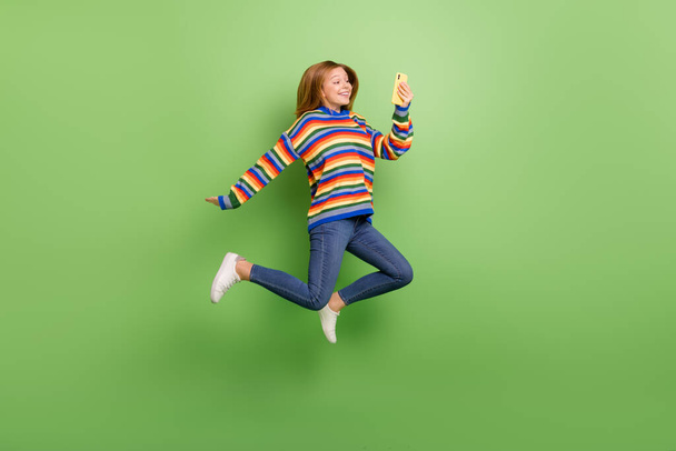Full length body size view of attractive cheerful funny girl jumping using device app isolated over bright green color background. - Photo, image