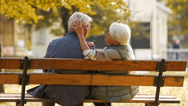 Старшая супружеская пара сидит на скамейке в парке, жена трогает мужей за волосы. Высокое качество фото - Фото, изображение
