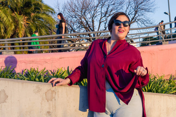 portrait young plus size latin caucasian argentinian woman, smiling with sunglasses and casual clothes, outdoors at sunset, looking at the camera. - Zdjęcie, obraz