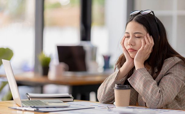 Een vrouwelijke startup werknemer ziet er gestrest uit van het werken de hele dag, ze is een boekhoudkundige en financiële werk in een bedrijf, ze is moe en gestrest, ze heeft office-syndroom. Hard werken concept. - Foto, afbeelding