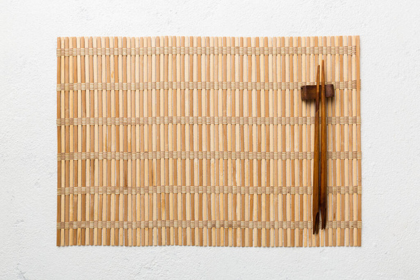 Dos palillos y estera de bambú sobre fondo de cemento. Vista superior, espacio de copia. - Foto, Imagen