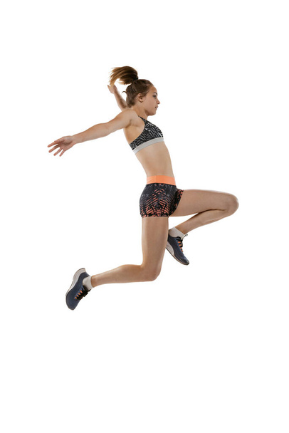 Long jump technique. Studio shot of professional female athlete in sports uniform jumping isolated on white background. Concept of sport, action, motion, speed, healthy lifestyle. Copy space for ad - Foto, Imagem